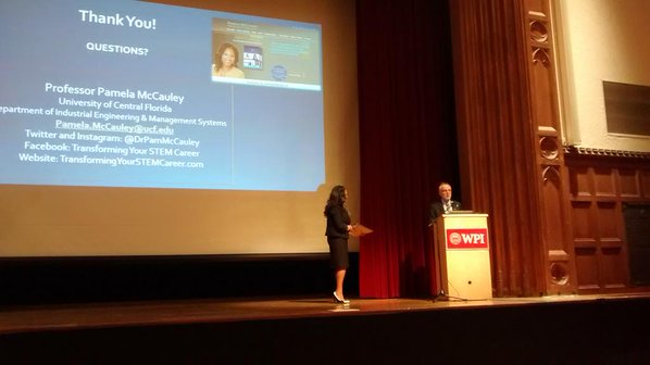 dr pamela mccauley giving a presentation standing on stage next to a man at a podium